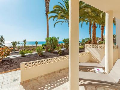 Sonniger Terrassenbereich mit Liegestuhl, Palmen und Blick aufs Meer unter blauem Himmel.