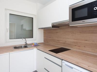 Moderne weiße Küche mit Holzarbeitsplatten, integriertem Herd, Mikrowelle und Spüle unter Fenster.
