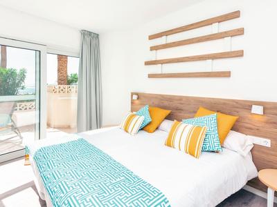 Helles Schlafzimmer mit Doppelbett, bunten Kissen, Holzkopfteil und Zugang zum Balkon mit Pflanzen.