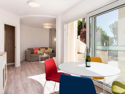 Helles Wohnzimmer mit bunten Stühlen, rundem Tisch, Sofa und großem Fenster mit Blick ins Grüne.