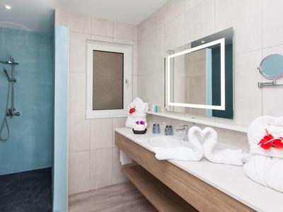 Modernes Badezimmer mit großer Dusche, beleuchtetem Spiegel und dekorativen Handtüchern in Herzform.