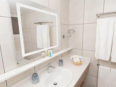 Helles Badezimmer mit weißem Waschbecken, Spiegel mit LED-Rahmen und Handtüchern an der Wand.