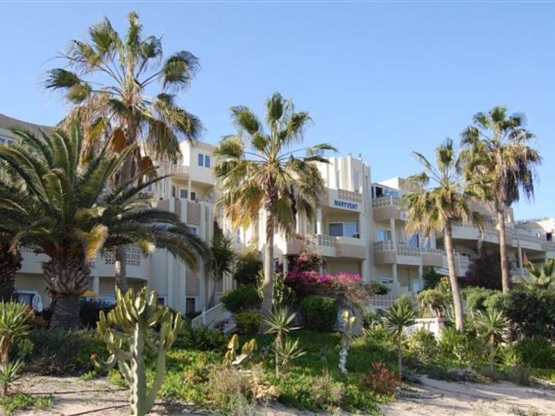 Wielopiętrowy hotel z balkonami otoczony palmami i zielenią pod czystym niebem.