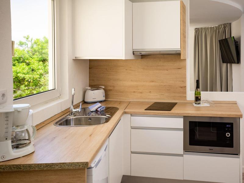 Nowoczesna kuchnia z drewnianymi blatami, białą zmywarką, mikrofalówką i ekspresem do kawy obok okna z widokiem na zieleń.