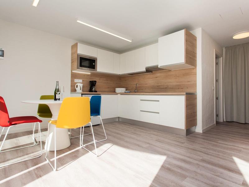 Nowoczesny aneks kuchenny z kolorowymi krzesłami i drewnianymi akcentami w jasnym apartamencie