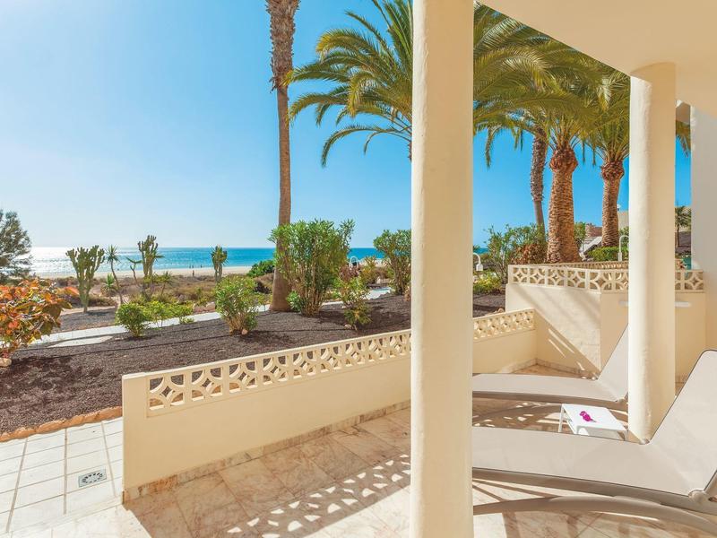 Zadaszony taras z leżakiem i widokiem na palmy oraz morze.