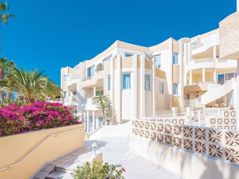 Nowoczesny biały kompleks hotelowy z niebieskimi oknami, kwitnącymi roślinami i czystym niebem