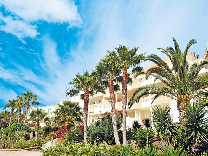 Budynek hotelu otoczony palmami i zielonymi roślinami pod niebieskim niebem