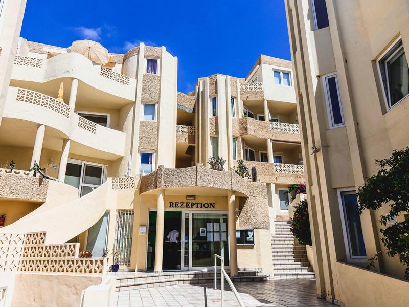 Jasna fasada hotelu z balustradami i wejściem do recepcji pod niebieskim niebem