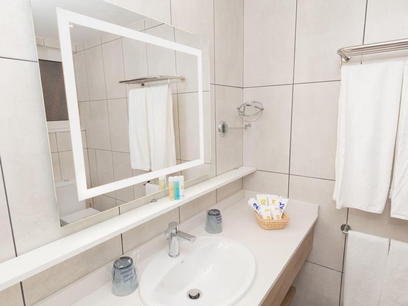 Jasna łazienka z umywalką, podświetlanym lustrem i ręcznikami na ścianie.