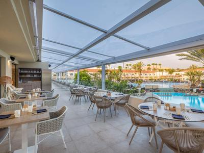 Offener Restaurantbereich mit Tischen und Stühlen neben einem Pool in einem Hotel.