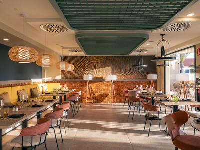 Modernes Hotelrestaurant mit hellem Holz, gelben Sitzbänken und hängenden Lampen.