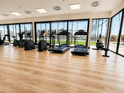 Großer Fitnessraum mit Holzfußboden und modernen Laufbändern an bodentiefen Fenstern.