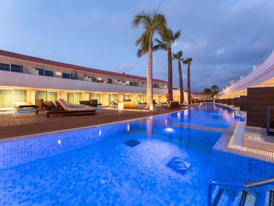 Moderner Hotelpool mit blauen Fliesen, Palmen und beleuchteter Terrasse bei Dämmerung.