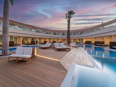Moderner Hotelpoolbereich mit Holzdeck, Palmen und bequemen Sitzmöbeln bei Sonnenuntergang.