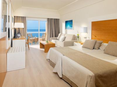 Modern hotel room with double bed, sofa, and balcony with sea view.