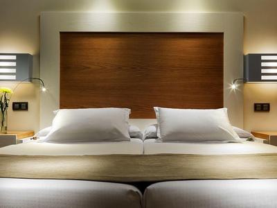 Modern hotel room with twin beds, wooden headboard, and soft ambient lighting.