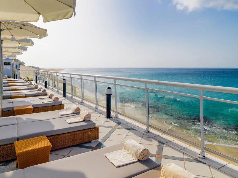 Sun loungers with towels on hotel terrace overlooking the sea under a blue sky.
