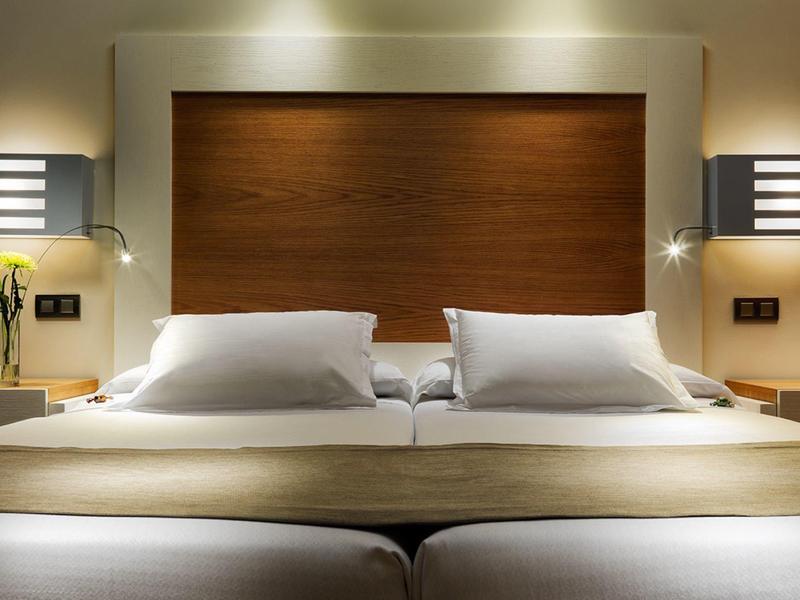 Modern hotel room with twin beds, wooden headboard, and soft ambient lighting.
