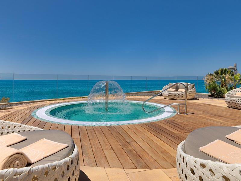 Oceanfront deck with a circular jacuzzi, wicker chairs, and a clear blue sky in the background.