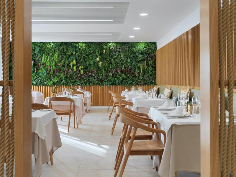 Modern restaurant with wooden chairs and green plant wall decor.