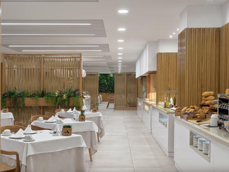 Modern breakfast room with white tables, wooden elements, and fresh pastries.