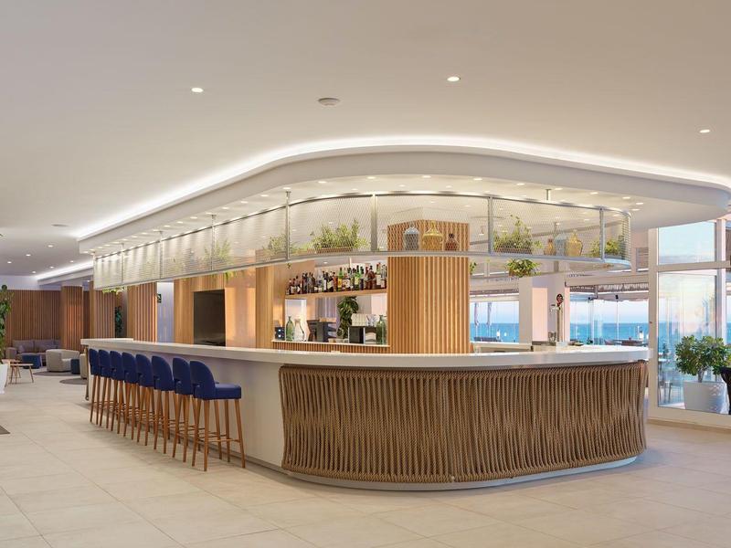 Bright, modern hotel bar area with curved wooden counter and blue bar stools.