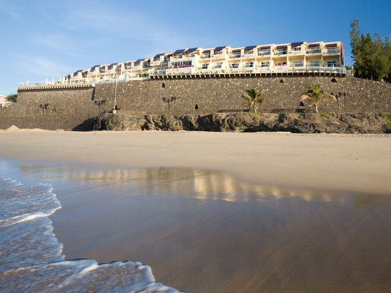 Hotel on a rocky beach with gentle waves and blue sky.