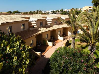 Bungalow a schiera circondati da palme e vegetazione sotto un cielo azzurro.