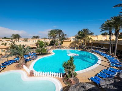 Grande piscina dell'hotel con sedie sdraio blu e palme sotto un cielo azzurro limpido.