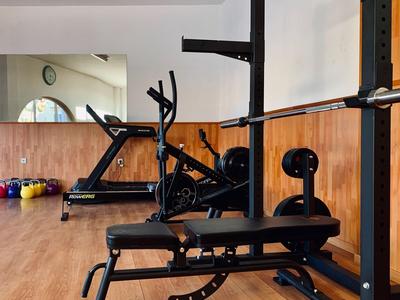 Piccola palestra con panca pesi, ellittica e kettlebell davanti a una parete in legno.