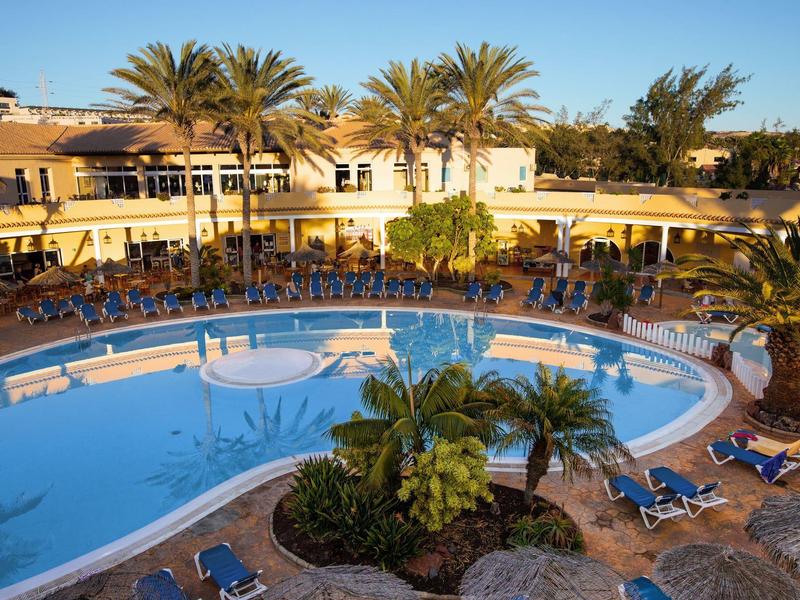 Piscina rotonda dell'hotel con lettini e palme in una struttura soleggiata.