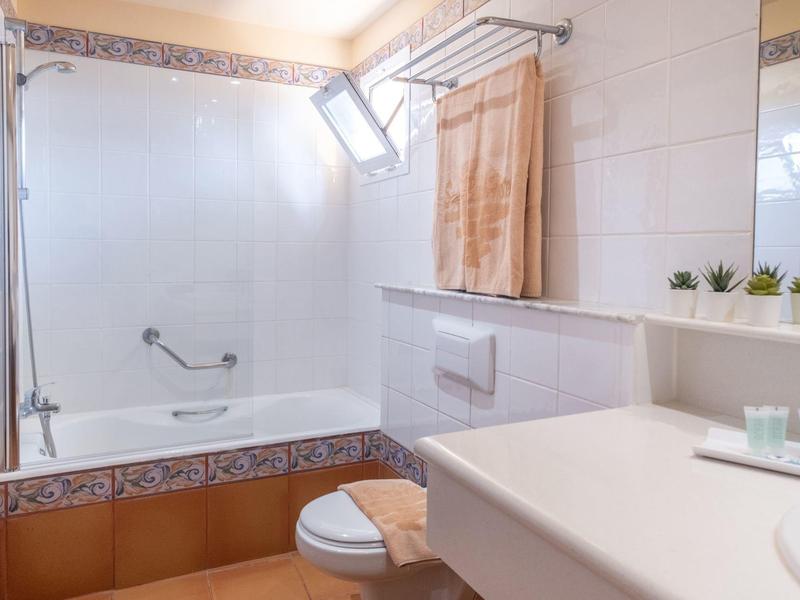 Bagno luminoso con vasca da bagno, WC, porta asciugamani e piccole piante su una mensola.