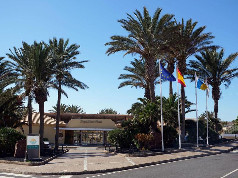 Edificio dell'hotel con diverse bandiere e palme sotto un cielo azzurro