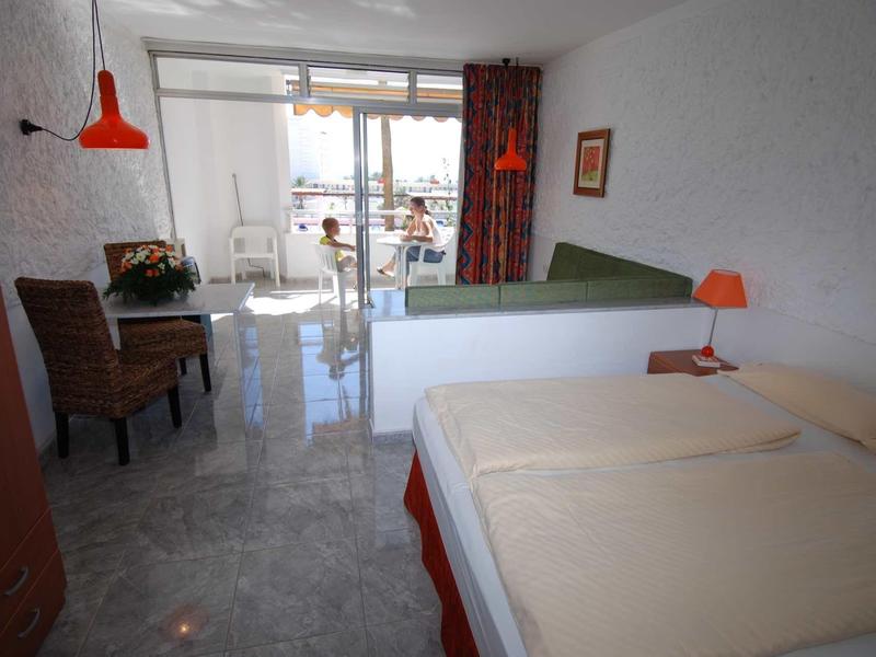 Hell eingerichtetes Zimmer mit Doppelbett, Schreibtisch, Stuhl und Balkon mit Blick nach außen.