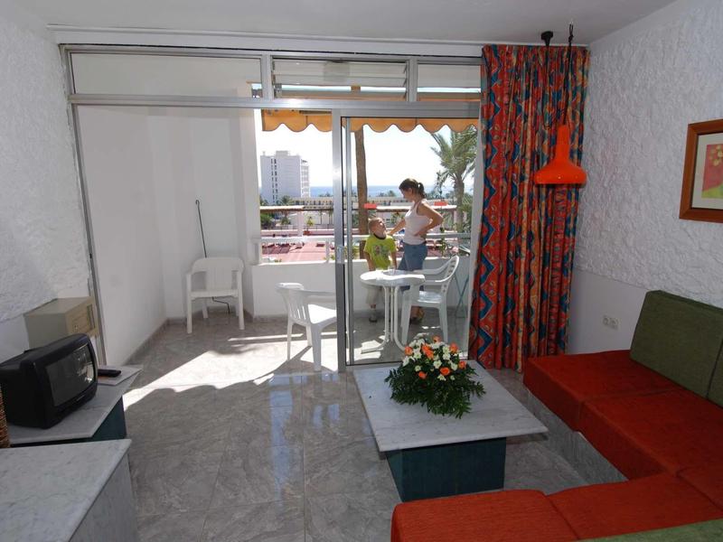 Hell eingerichtetes Wohnzimmer mit rotem Sofa, kleinem Fernseher und Balkon mit Stadtblick.