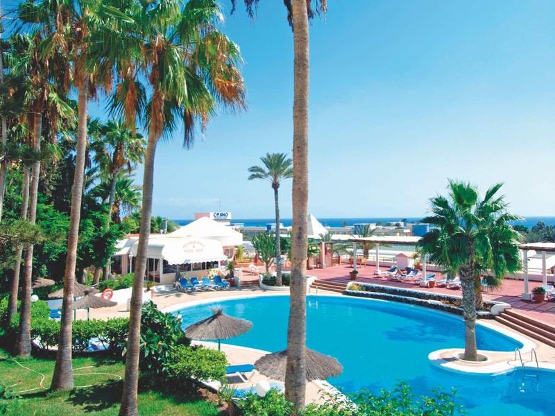 Palmen umgeben einen blauen Pool in einer sonnigen und grünen Resortlandschaft.