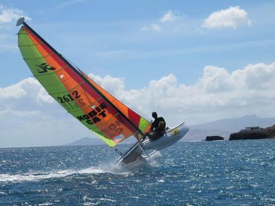 Ein Windsurfer auf blauem Wasser mit buntem Segel unter klarem Himmel.