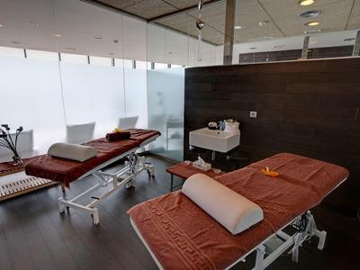 Behandlungsraum mit zwei braunen Massageliegen, weißen Handtüchern und modernem Ambiente.