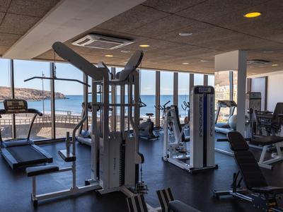 Helles Fitnessstudio mit modernen Geräten und großer Fensterfront mit Meerblick.