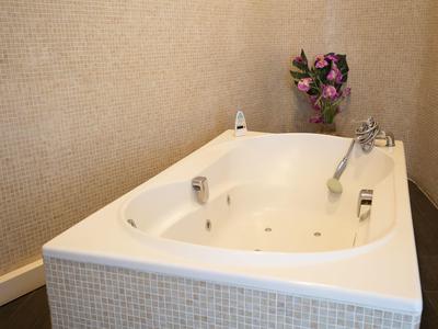Weiße Badewanne mit Chromarmaturen und lila Blumen vor beige gestrichener Wand.