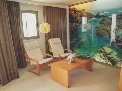 Kleines Zimmer mit zwei bequemen Stühlen, Holztisch und großem Fenster mit Vorhängen.