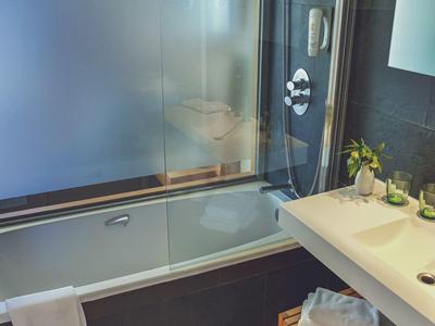 Modernes Badezimmer mit weißer Badewanne, Glasdusche, Handtuch und Holzgitterregal unter Waschbecken.