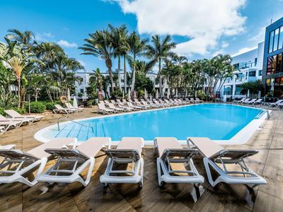 Duży basen hotelowy z leżakami i palmami w słoneczny dzień.