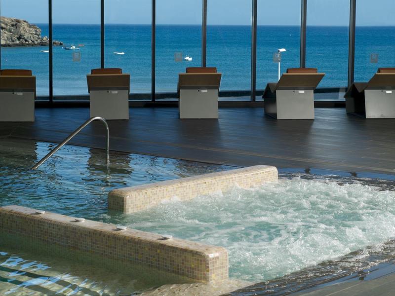 Binnenzwembad met bruisend water en grote ramen met uitzicht op de oceaan en het strand.