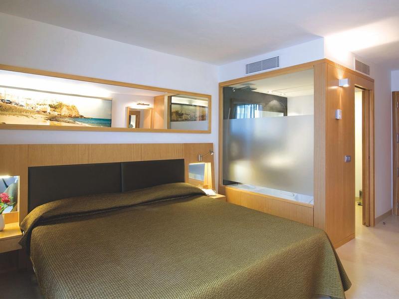 Modern hotelkamer met tweepersoonsbed, grote spiegel en matglazen afscheiding bij badkamer.