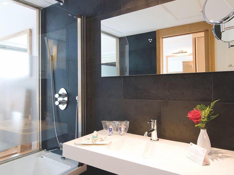 Moderne hotelbadkamer met zwarte tegels, grote spiegel, witte wastafel en netjes opgevouwen handdoeken.