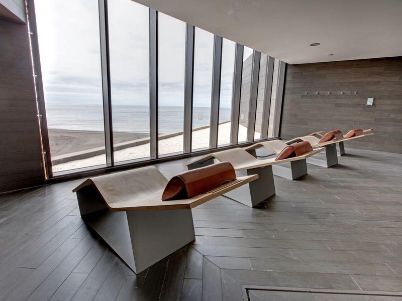 Moderne lounge met hoekige banken en grote ramen met uitzicht op zee.