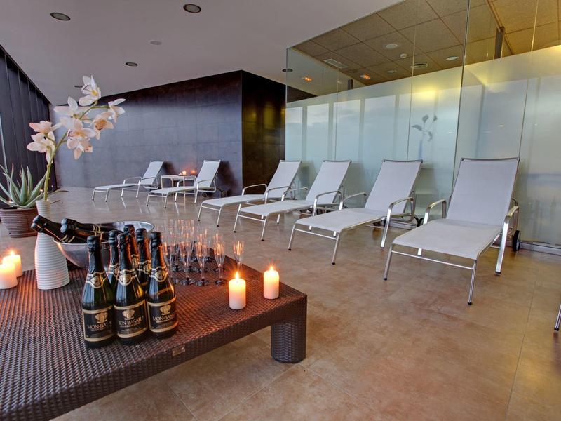 Overdekte ontspanningsruimte met ligstoelen, kaarsen en drankjes op een bruine tafel.