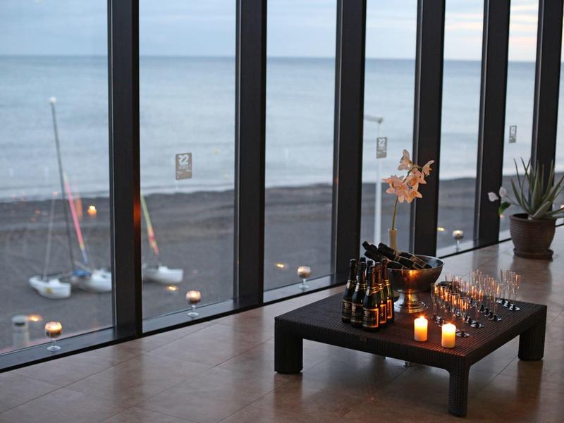 Moderne kamer met grote ramen aan de vloer, uitzicht op de oceaan, salontafel met brandende kaarsen en schaakspel.